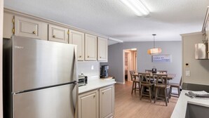 A modern kitchen with a stainless steel refrigerator, wooden cabinets, a dining area with a table and chairs, and a pendant light. - Lake it Easy Private Dock with fish cleaning station (Batesburg-Leesville)