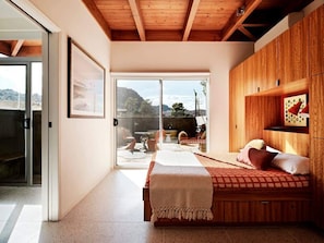 Ein Schlafzimmer mit einem Bett, Holzboden, einer Schiebetür zu einer Terrasse und einem gerahmten Bild an der Wand.