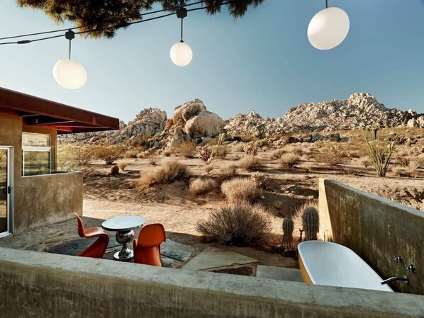 An outdoor seating area with a table and chairs, a bathtub, and a view of a rocky landscape.