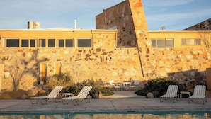 A pool area with lounge chairs, a stone building, and a clear sky. - Radziner Modernist Cabin By Homestead Modern (Joshua Tree)