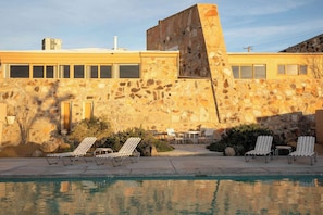 Ein Poolbereich mit Liegestühlen, ein Steinhaus und ein klarer Himmel.