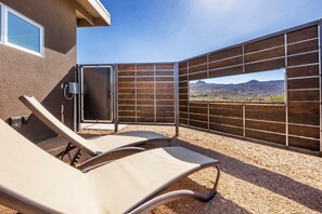 Eine Terrasse mit zwei Liegestühlen, einem Metallzaun und Blick auf Berge.