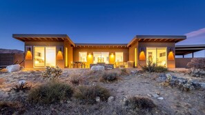 A modern two-story building with large windows and doors, a patio area with outdoor seating, and a desert landscape. - Shelter 2 By Homestead Modern (Joshua Tree)