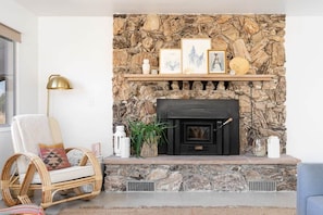 A stone fireplace with a mantel shelf, a wicker chair, and a floor lamp. - Sommer Ranch By Homestead Modern (Yucca Valley)