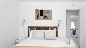 A bedroom with a wooden headboard, a bed with white bedding, two bedside lamps, and a wall-mounted abstract artwork. - Sommer Ranch By Homestead Modern (Yucca Valley)
