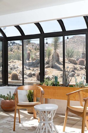 Conservatório com vista para cactos do deserto, móveis de madeira e uma mesa branca.