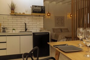 A compact kitchen with a microwave, sink, and small refrigerator. There is a dining area with a table, chairs, and wine glasses. - Iuman Patagonia (El Calafate)