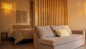 A bedroom with a bed, a sofa, a wooden slat partition, and a wall-mounted light fixture. - Iuman Patagonia (El Calafate)