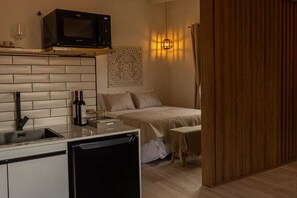 A compact hotel room with a kitchenette, a bed with a headboard, a bedside table, and a wall-mounted light fixture. - Iuman Patagonia (El Calafate)