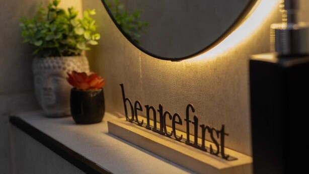 A wall-mounted sign with the words 'benicefirst' and a potted plant with a red flower to the left. - Iuman Patagonia (El Calafate)