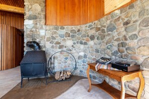A stone wall, a wood-burning stove, a table with a record player, and a metal chair. - Maine Country Escape with Private Pond Views (Holden)