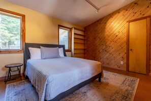 A bedroom with a bed, a small stool, a window, and a door. - Maine Country Escape with Private Pond Views (Holden)