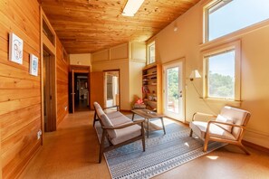 A wooden interior with a sofa, chairs, a table, and a bookshelf. - Maine Country Escape with Private Pond Views (Holden)
