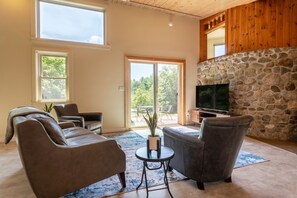 Ein Wohnzimmer mit Kamin aus Stein, Ledersofas, einem Fernseher und großen Fenstern.