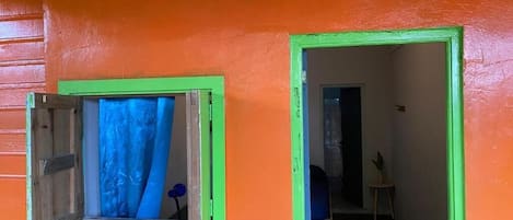 Ein Zimmer mit Fenster und Tür, beide mit grünen Rahmen, und einer Pflanze auf der linken Seite.