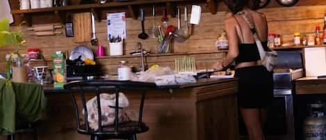 Una cocina con barra de madera, taburetes, ollas colgantes y un cartel en la pared.