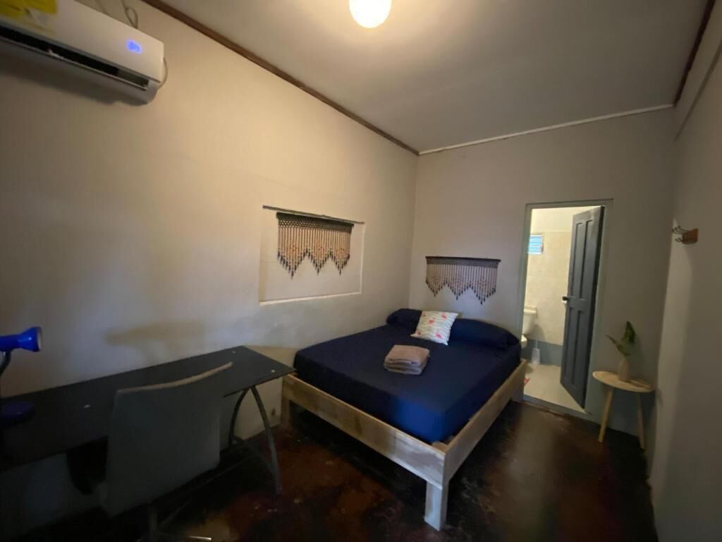 A bedroom with a bed, a desk, an air conditioning unit, and a door leading to another room.