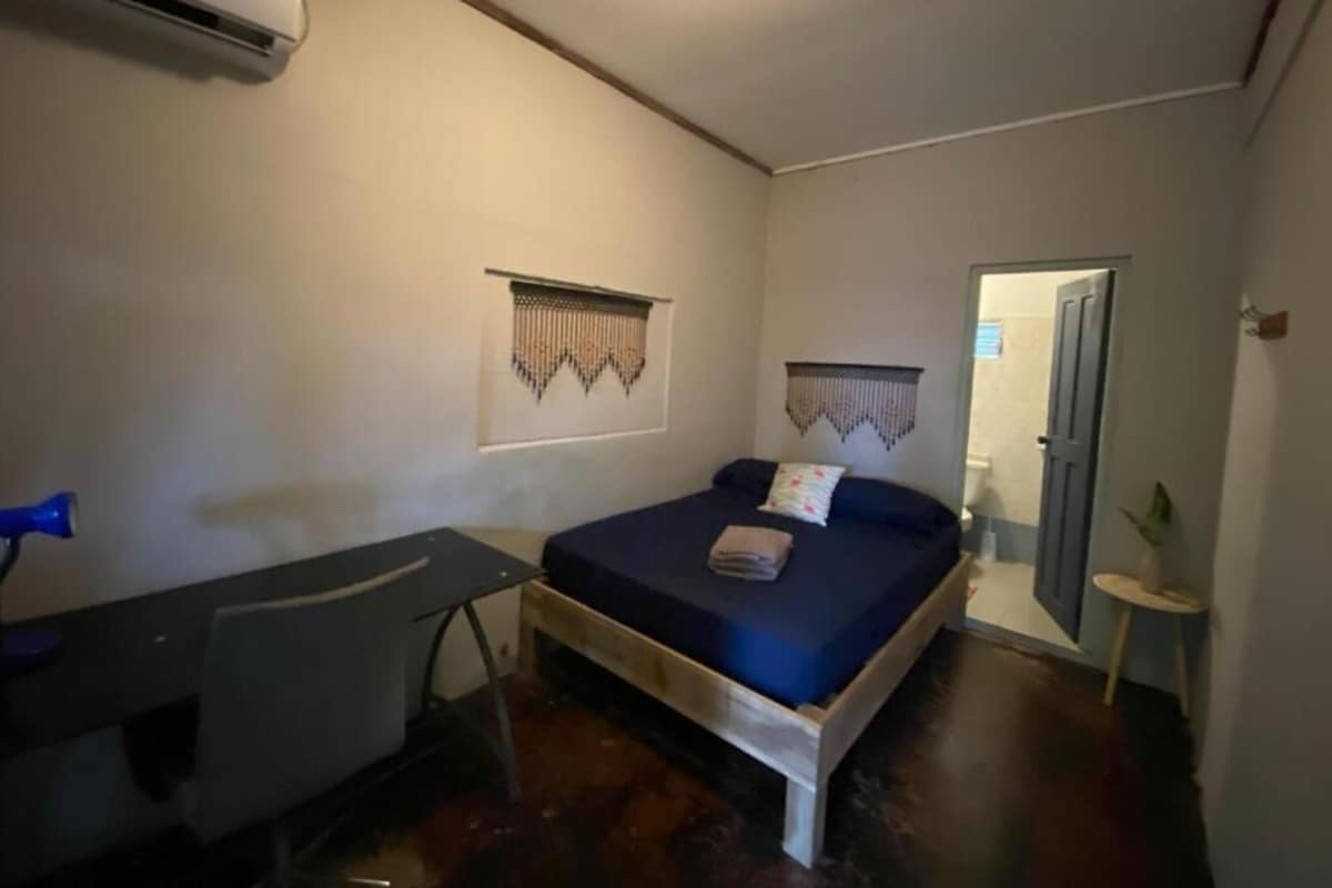 Une chambre à coucher comprenant un lit, un bureau, un appareil de climatisation et une porte donnant sur une autre pièce.