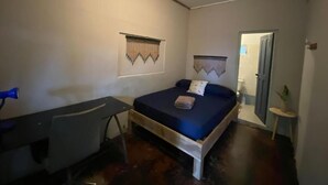 A bedroom with a bed, a desk, an air conditioning unit, and a door leading to another room. - Hostel Bocas Estrella (Bocas del Toro)