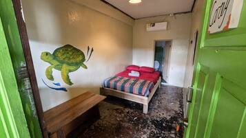Quarto com cama, um mural na parede, um banco e uma porta com um aviso.