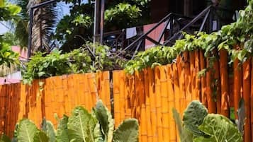 Un barrio residencial con cerca de bambú, plantas grandes y frondosas, y un edificio de techo inclinado.
