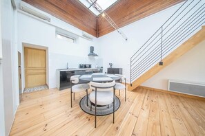 A modern kitchen with a central island, a dining area with a round table and chairs, and a wooden staircase. - La pépite : écrin historique au bord de l'eau (Quimper)