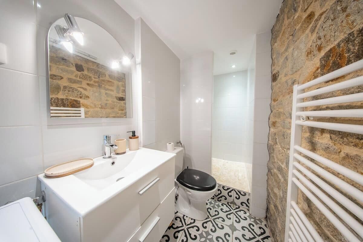 Un bany amb un lavabo blanc, un mirall, un vàter i una dutxa.
