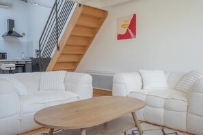 Ein modernes Wohnzimmer mit einer Holztreppe, weißen Sofas und einem Gemälde an der Wand.