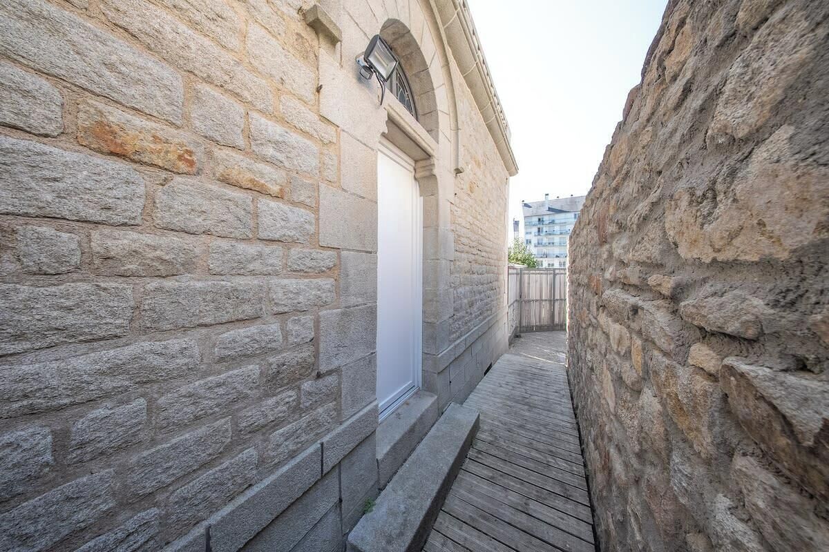 A narrow stone corridor with a wooden deck leading to a building entrance.