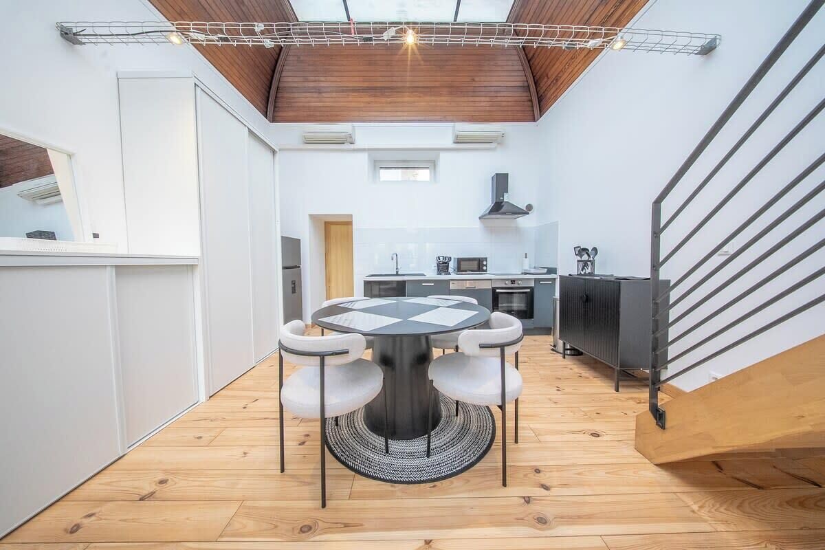Eine moderne Küche mit Kochinsel, ein Essbereich mit rundem Tisch und eine Treppe, die in eine obere Etage führt.