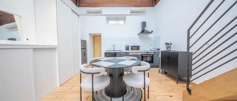 Eine moderne Küche mit Kochinsel, ein Essbereich mit rundem Tisch und eine Treppe, die in eine obere Etage führt.