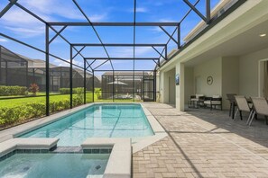 Ein Schwimmbad mit Glasveranda, umgeben von einer Terrasse mit Stühlen und einem kleinen Tisch.