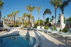 Un área de piscina con sillones reclinables y palmeras.