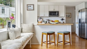 A kitchen with white cabinets, a microwave, a refrigerator, and a dining area with stools.