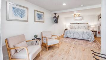 A bedroom with a bed, two chairs, a small table with a plant, and two framed artworks on the wall.