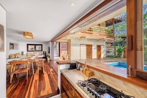 A modern kitchen with a large island, wooden flooring, and a view of a swimming pool. - Deluxe 2-Bedroom Family Suite at Villa Luz Do Mar (Jijoca de Jericoacoara)