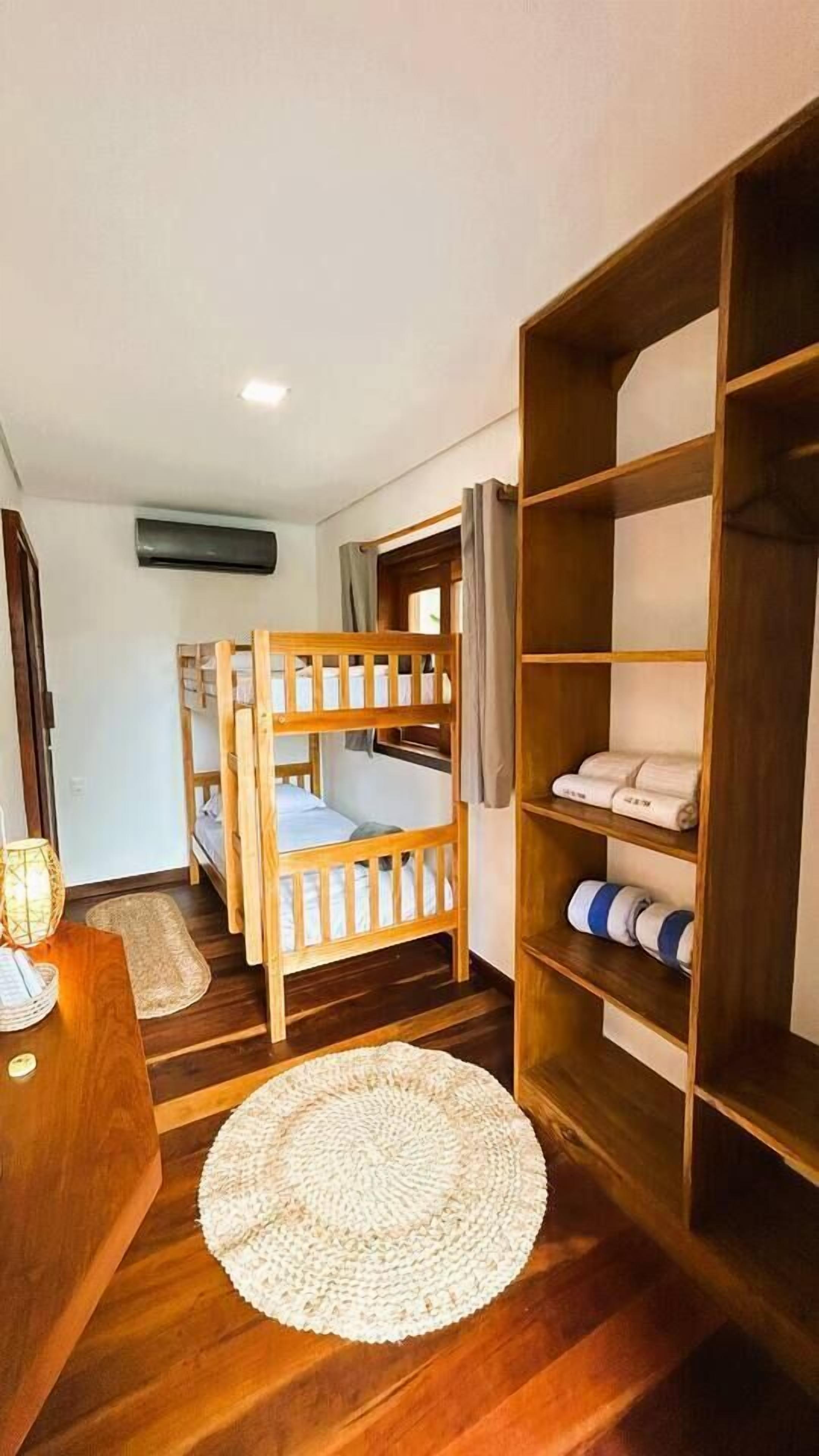 A room with a bunk bed, a wooden wardrobe, a woven mat, and a small table.
