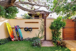 A garden with a wooden fence, a thatched-roof structure, and two surfboards leaning against the wall. - Deluxe 2-Bedroom Family Suite at Villa Luz Do Mar (Jijoca de Jericoacoara)