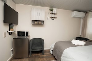 A hotel room with a bed, a desk with a microwave, a chair, a TV mounted on the wall, and a small shelf with decorative items. - Ninho de Setúbal - Studio for solo travelers (São Lourenço)