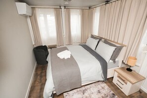 Ett sovrum med en säng, ett nattduksbord, en lampa och gardiner.