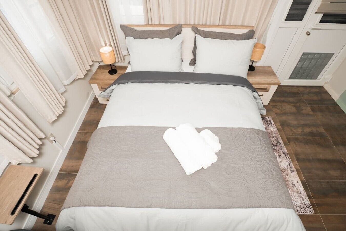 A neatly made bed with a grey and white duvet, two bedside lamps, and a wooden nightstand.