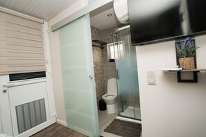 A modern bathroom with a glass shower enclosure, a toilet, and a built-in TV. - Ninho de Setúbal - Studio for solo travelers (São Lourenço)