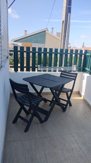 A balcony with a table and chairs, a green fence, and a building in the background. - Ninho de Setúbal - Studio for solo travelers (São Lourenço)