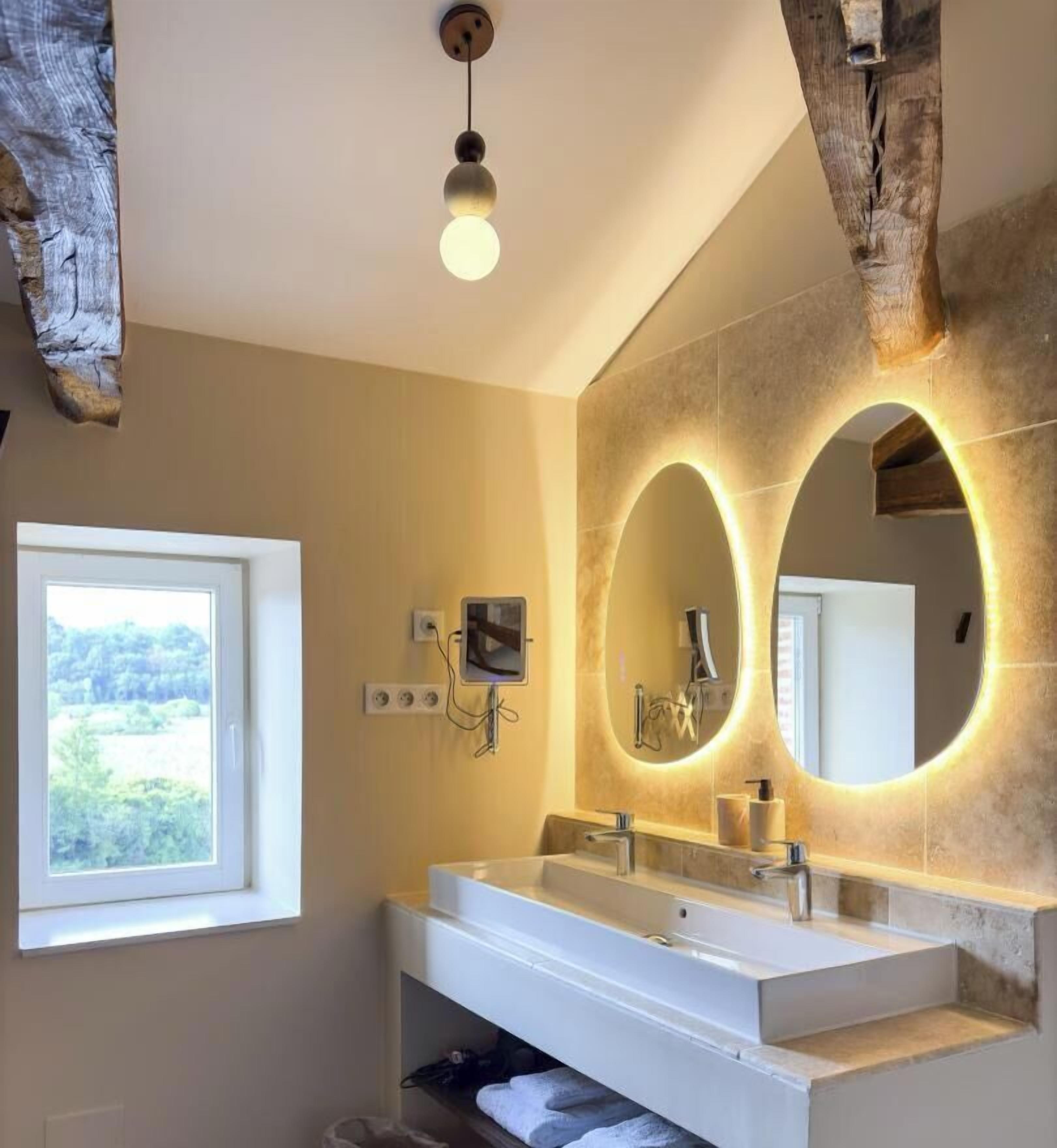 Ein Badezimmer mit einem weißen Waschbecken, zwei Spiegeln und einem Fenster.