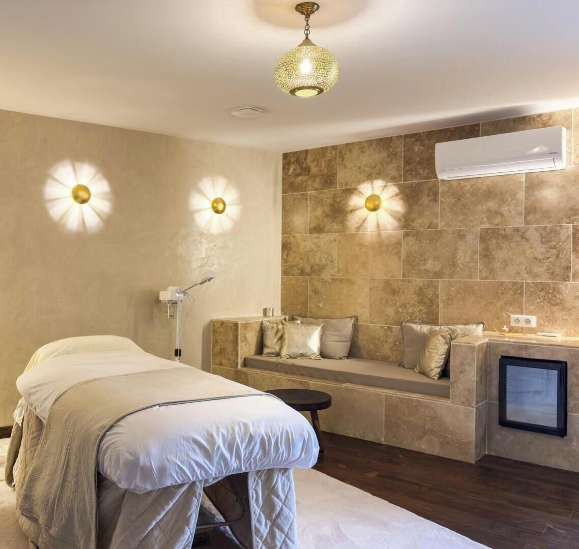 A modern bedroom with a bed, a bedside table, a massage chair, and a wall-mounted air conditioner.