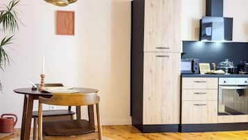 Een moderne keuken met houten kastjes, een eethoek met een ronde tafel en stoelen, en een hangende lamp.
