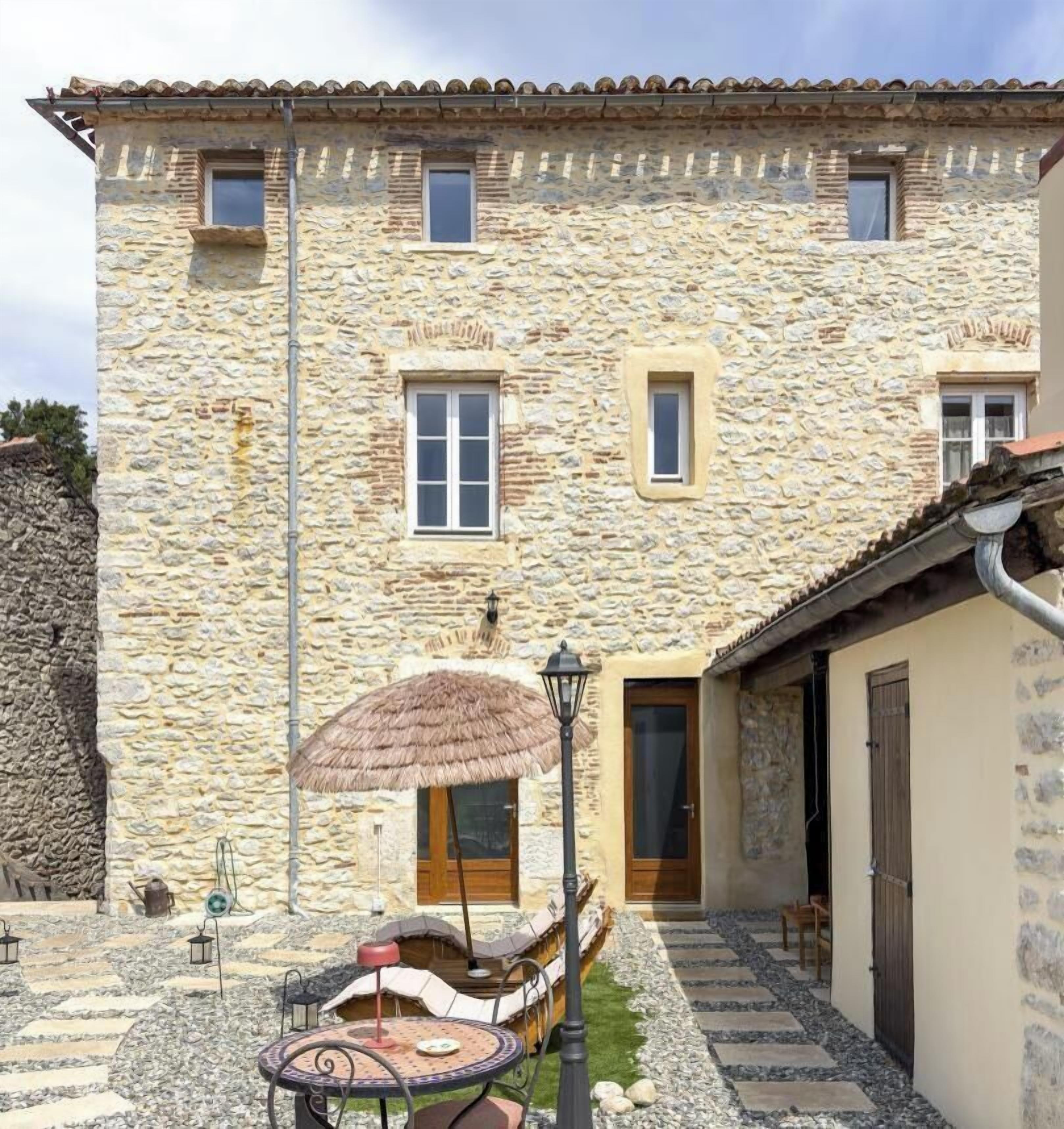 A stone building with a courtyard, a thatched umbrella, and outdoor seating.