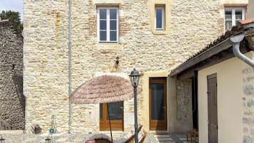 A stone building with a courtyard, a thatched umbrella, and outdoor seating.