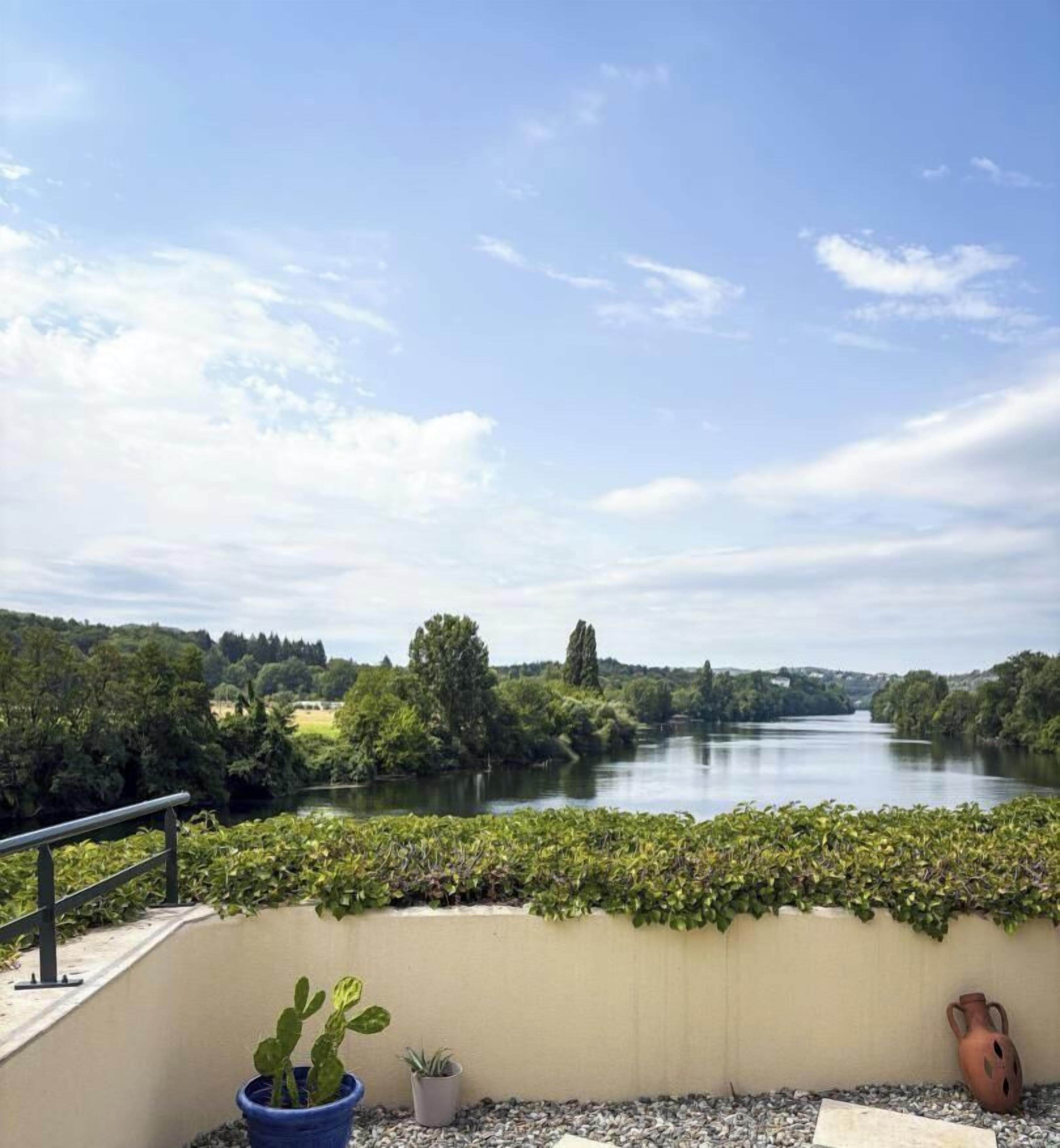 Een balkon met uitzicht op een rivier, met bloempotten en een decoratieve vaas.