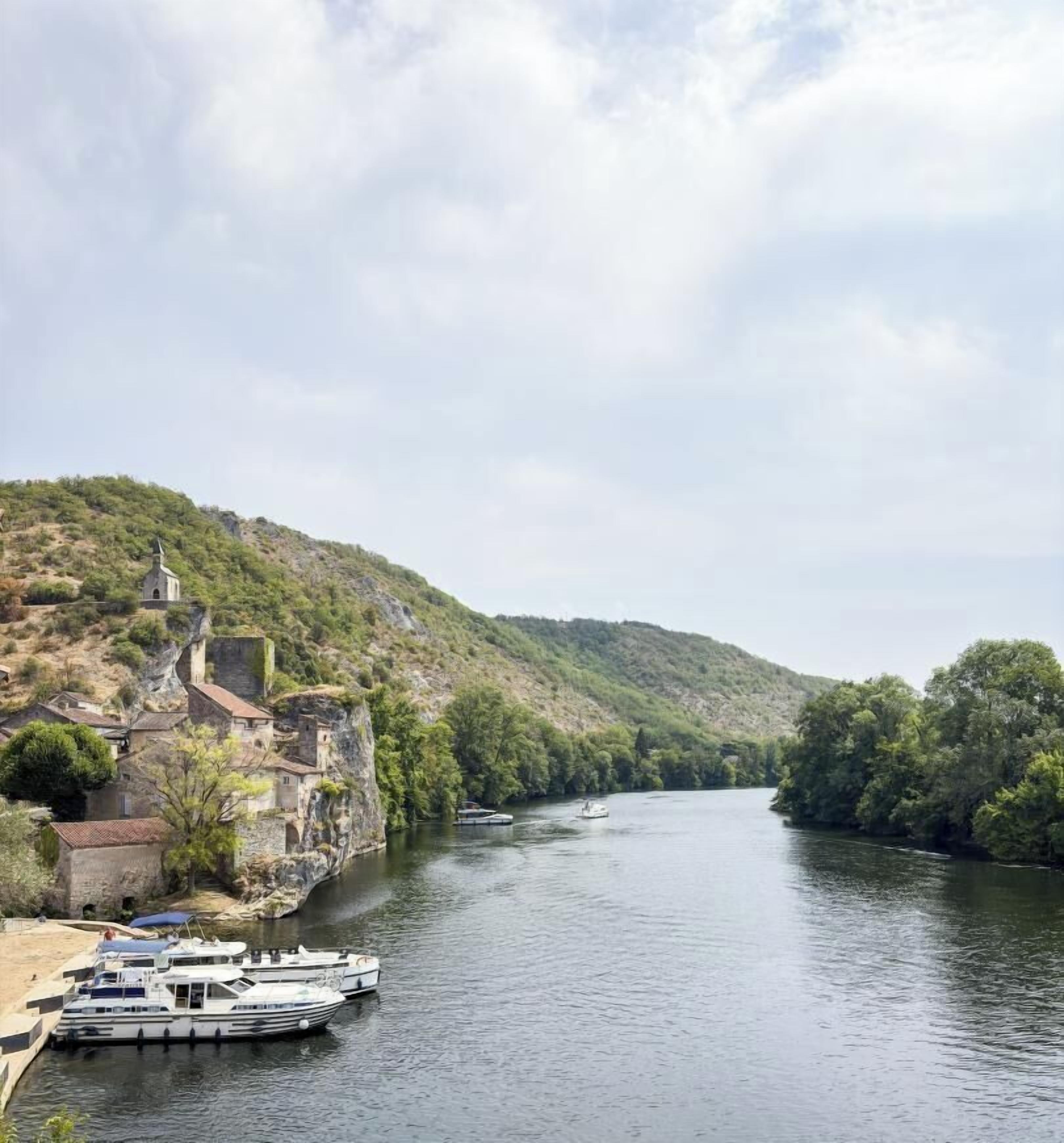 A river with boats docked, a building on a hill, and a clear sky.